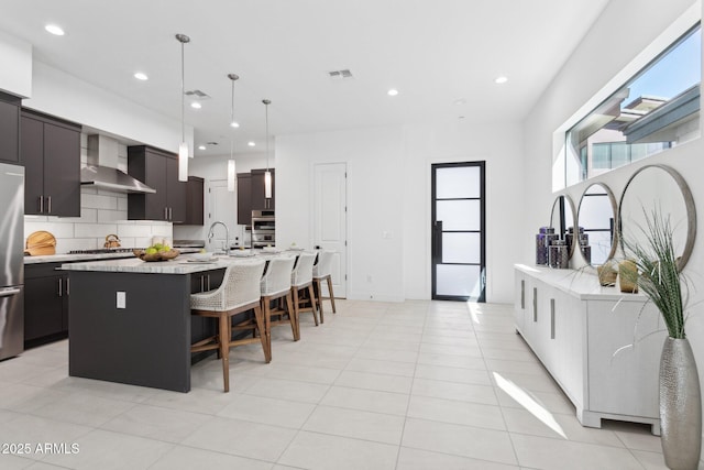 kitchen with a large island, a kitchen breakfast bar, recessed lighting, wall chimney exhaust hood, and stainless steel appliances