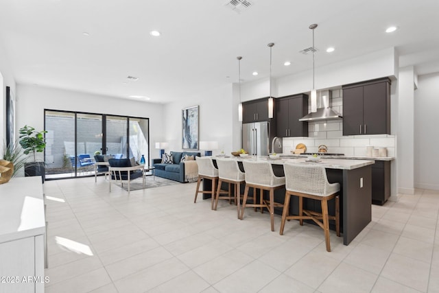 kitchen featuring high end refrigerator, a breakfast bar area, wall chimney exhaust hood, and visible vents