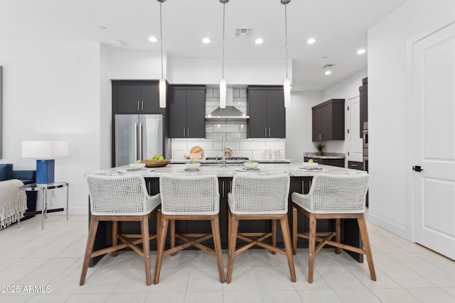 kitchen with wall chimney range hood, a breakfast bar, a center island with sink, and high end refrigerator