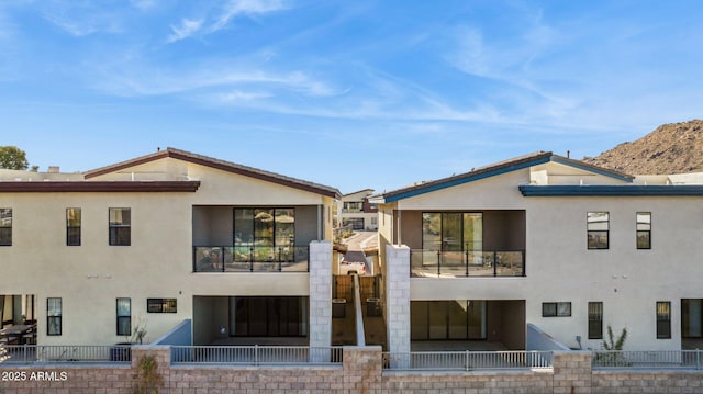 back of property with stucco siding, a balcony, and fence