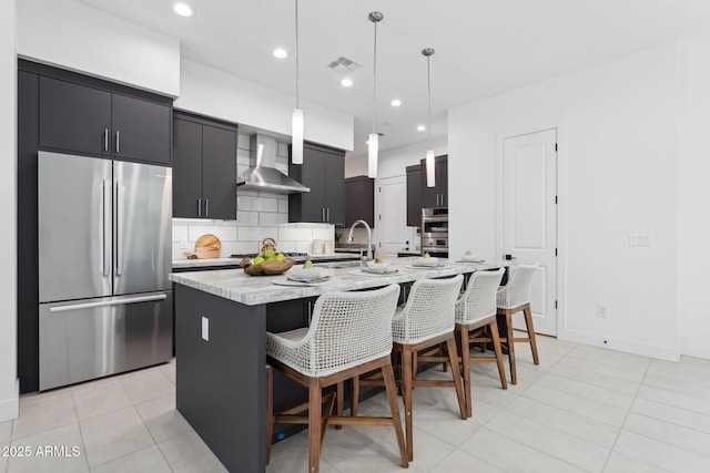 kitchen with visible vents, a breakfast bar, wall chimney range hood, a sink, and stainless steel appliances
