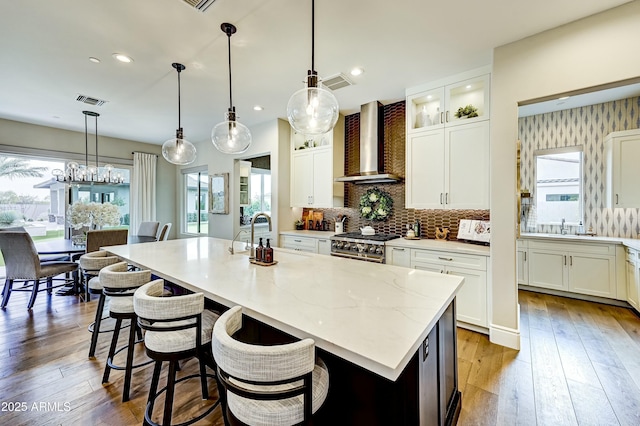 kitchen featuring an island with sink, wall chimney exhaust hood, and decorative light fixtures