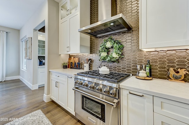 kitchen with white cabinetry, wall chimney range hood, high end range, and light stone countertops