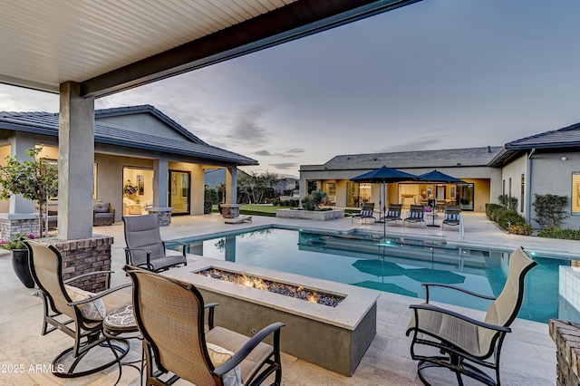 pool at dusk with a patio and a fire pit