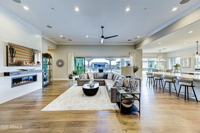 living room featuring ceiling fan with notable chandelier, ornamental molding, a tile fireplace, and light hardwood / wood-style flooring