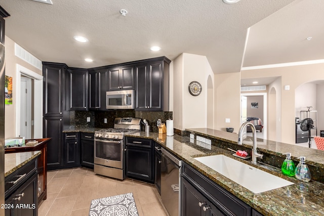 kitchen with tasteful backsplash, sink, stainless steel appliances, dark stone countertops, and light tile patterned floors