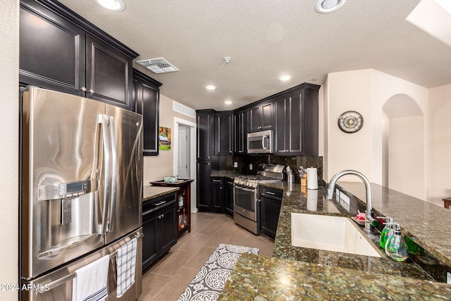 kitchen featuring decorative backsplash, dark stone countertops, stainless steel appliances, and sink