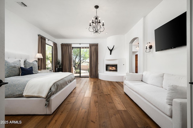 7025 E Ashler Hills Dr, Scottsdale, AZ 85266 - bedroom featuring access to outside, a chandelier, a glass covered fireplace, wood-type flooring, and arched walkways