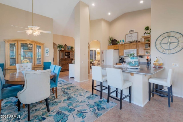 dining area with light tile patterned floors, visible vents, arched walkways, baseboards, and high vaulted ceiling