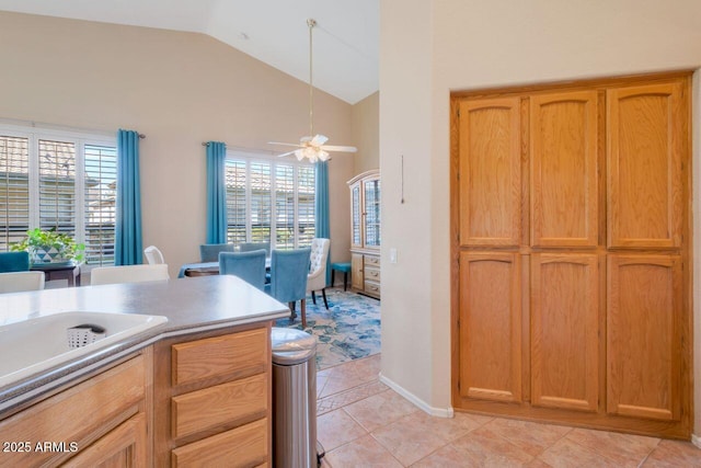 kitchen featuring light countertops, a ceiling fan, brown cabinetry, light tile patterned flooring, and vaulted ceiling