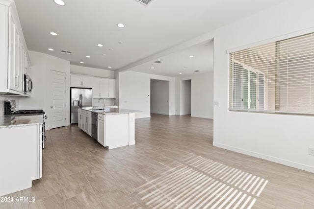 kitchen with a kitchen island with sink, appliances with stainless steel finishes, white cabinetry, and light stone counters