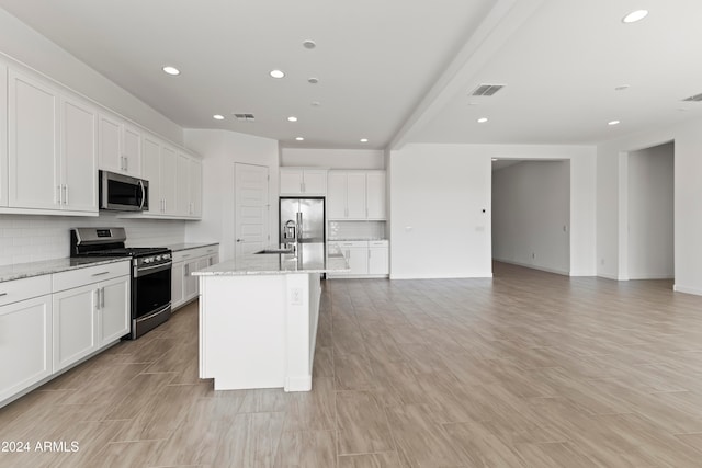 kitchen featuring white cabinetry, appliances with stainless steel finishes, backsplash, light stone countertops, and a kitchen island with sink