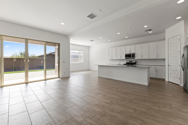 kitchen with light stone counters, appliances with stainless steel finishes, an island with sink, white cabinets, and decorative backsplash