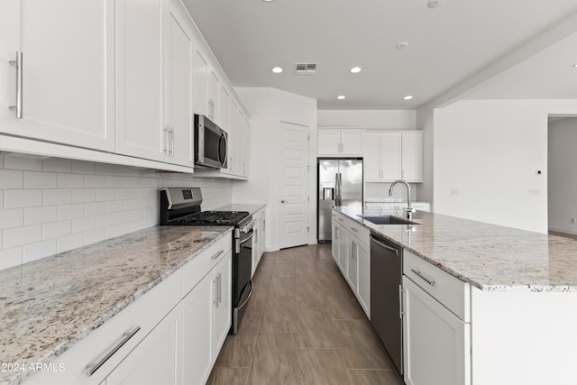 kitchen featuring stainless steel appliances, light stone countertops, sink, white cabinets, and a kitchen island with sink