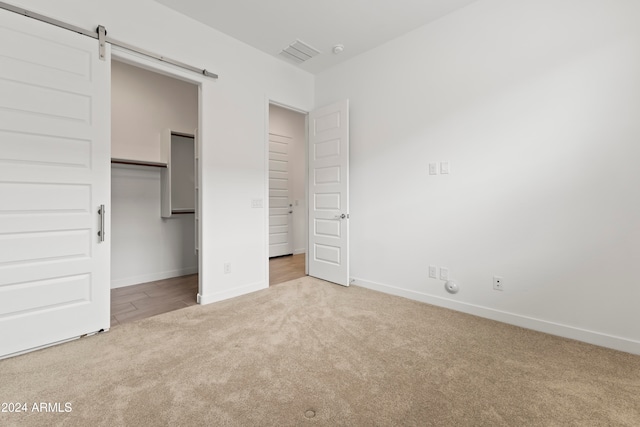 unfurnished bedroom featuring light carpet, a barn door, and a closet