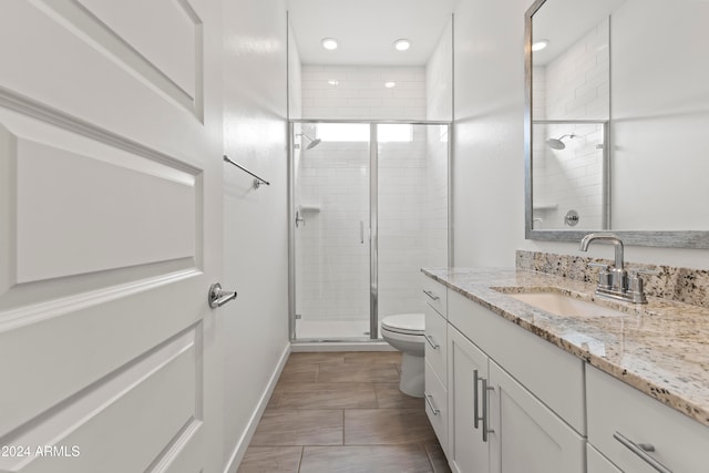 bathroom featuring a shower with door, vanity, and toilet