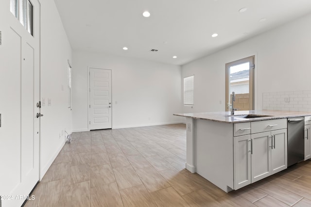 kitchen featuring stainless steel dishwasher, sink, and light stone counters