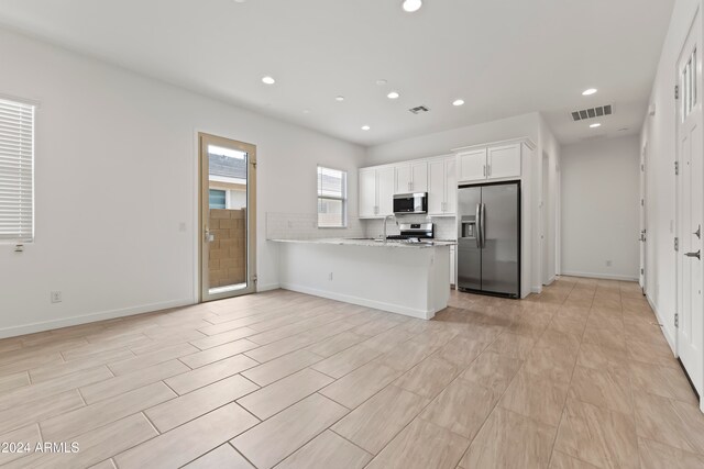 kitchen with stainless steel appliances, light stone counters, white cabinets, kitchen peninsula, and sink