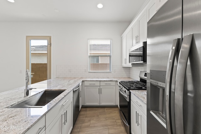 kitchen with light stone countertops, appliances with stainless steel finishes, sink, and white cabinets