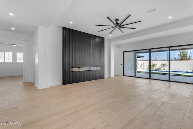 spare room with a large fireplace, visible vents, a ceiling fan, and wood finished floors