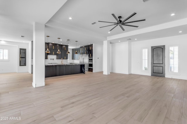 unfurnished living room featuring plenty of natural light, a sink, light wood-style flooring, and recessed lighting