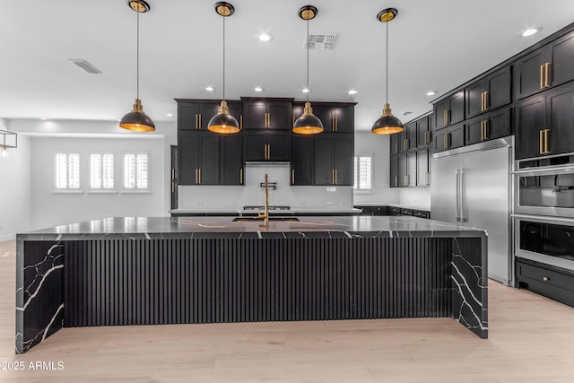 kitchen featuring stainless steel appliances, dark stone countertops, a large island with sink, and visible vents