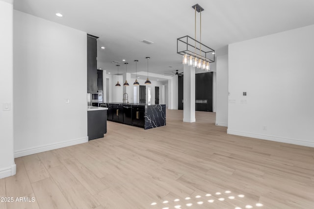 kitchen featuring visible vents, light wood-style flooring, open floor plan, dark cabinetry, and ceiling fan with notable chandelier