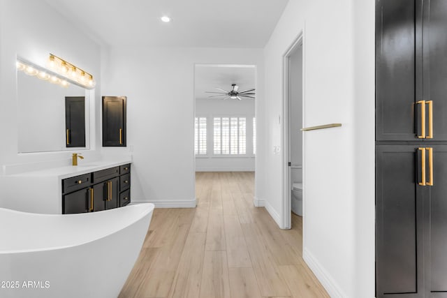 hallway featuring recessed lighting, a sink, light wood-style flooring, and baseboards