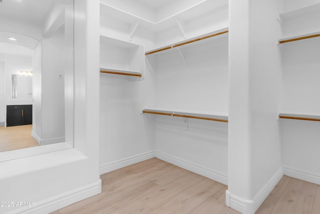 walk in closet with arched walkways and wood finished floors