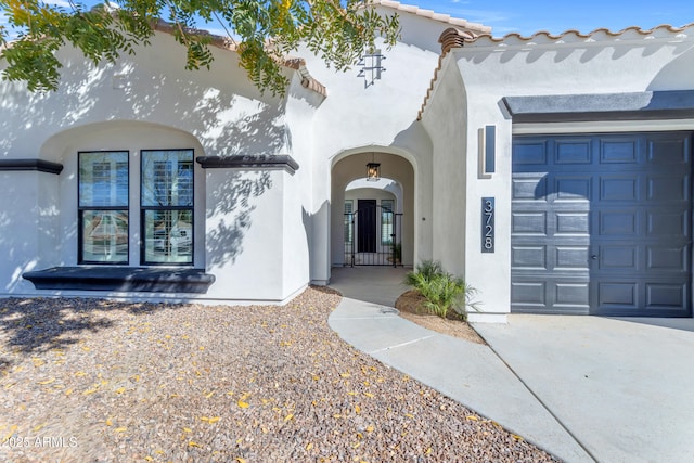 entrance to property featuring a garage, a tile roof, and stucco siding