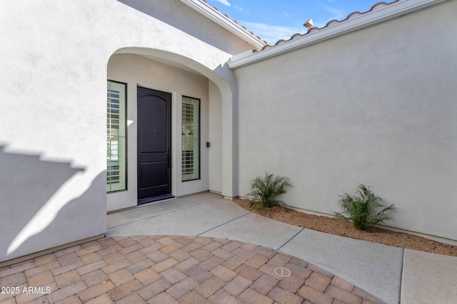 doorway to property with a patio area, a tiled roof, and stucco siding