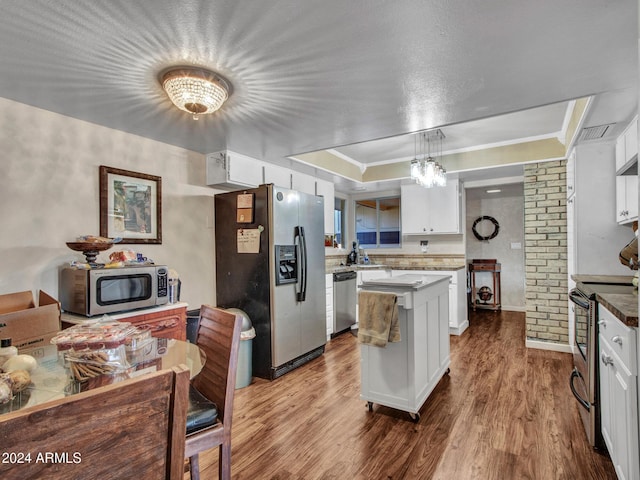 kitchen with hardwood / wood-style floors, hanging light fixtures, a tray ceiling, white cabinetry, and stainless steel appliances