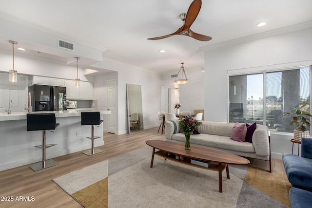 living room with baseboards, visible vents, crown molding, light wood-style floors, and recessed lighting