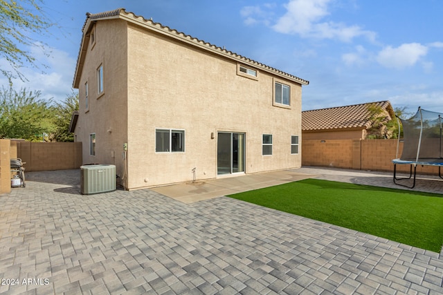 rear view of property with a yard, a trampoline, a patio, and central AC unit