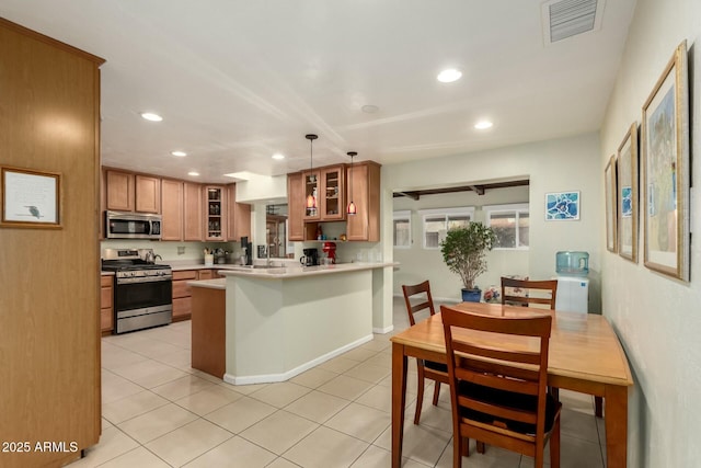 kitchen featuring stainless steel appliances, a peninsula, visible vents, brown cabinets, and glass insert cabinets