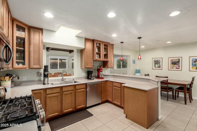 kitchen featuring stainless steel appliances, brown cabinetry, a sink, and a peninsula