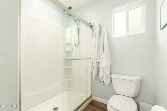 bathroom with a stall shower, baseboards, toilet, and wood finished floors