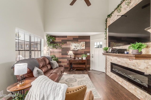 living room with a high ceiling, a stone fireplace, wooden walls, dark hardwood / wood-style floors, and ceiling fan