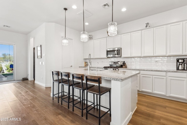 kitchen featuring stainless steel appliances, tasteful backsplash, visible vents, and wood finished floors