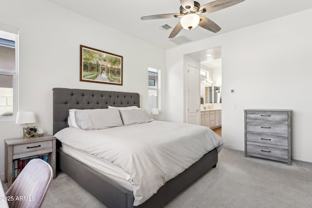 bedroom featuring ensuite bathroom, light colored carpet, a ceiling fan, baseboards, and visible vents