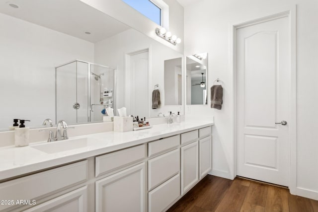 full bathroom with double vanity, a ceiling fan, a sink, a shower stall, and wood finished floors