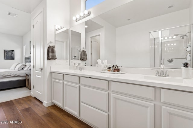 ensuite bathroom with double vanity, a stall shower, visible vents, and wood finished floors