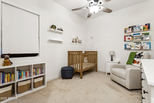 bedroom with baseboards, ceiling fan, a crib, and light colored carpet