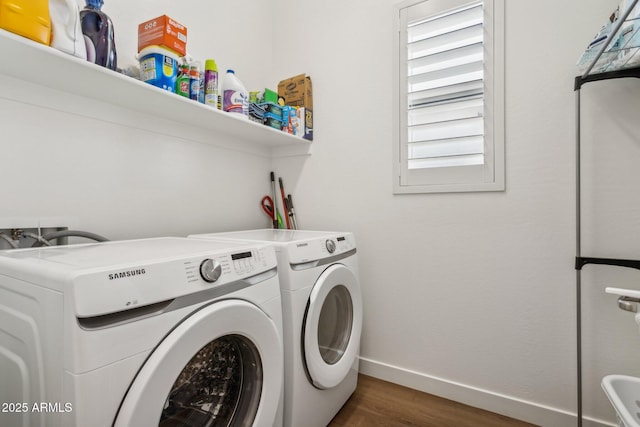 clothes washing area with laundry area, wood finished floors, washing machine and clothes dryer, and baseboards