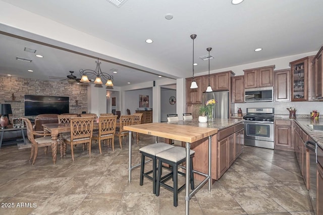 kitchen with pendant lighting, butcher block countertops, stainless steel appliances, a kitchen breakfast bar, and decorative backsplash