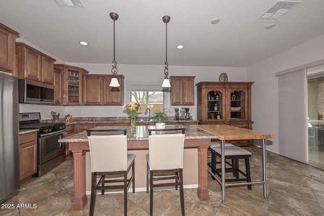 kitchen featuring stainless steel appliances, a kitchen island, light stone counters, and a kitchen bar