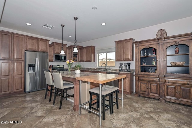 kitchen featuring a kitchen island, appliances with stainless steel finishes, butcher block counters, sink, and hanging light fixtures