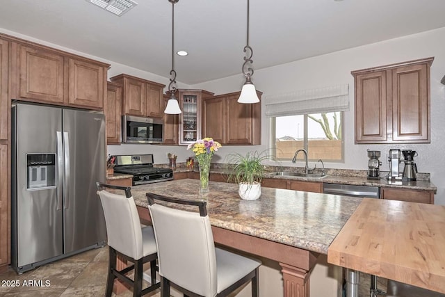 kitchen featuring pendant lighting, sink, appliances with stainless steel finishes, a center island, and light stone counters