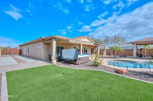 rear view of property with a hot tub, a patio area, and a lawn