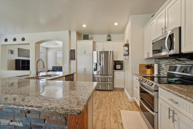 384 N Scott Dr, Chandler, AZ 85225 - kitchen featuring light stone counters, stainless steel appliances, a sink, arched walkways, and light wood-type flooring